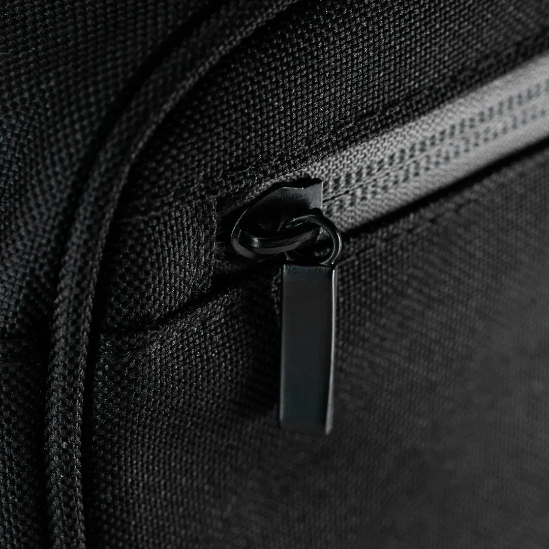 Eine extreme Nahaufnahme eines eleganten schwarzen Metall-Reißverschlusses und des strukturierten, wasserabweisenden Canvas-Materials der Tasche.