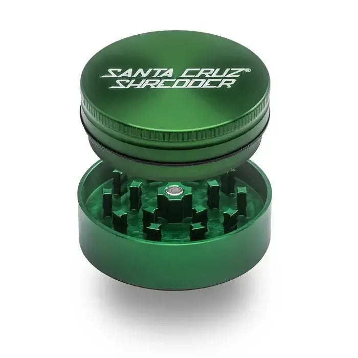 Ein grüner, zweiteiliger Santa Cruz Shredder Kräuter-Grinder, dessen magnetischer Deckel über den scharfen, rautenförmigen Mahlzähnen schwebt.