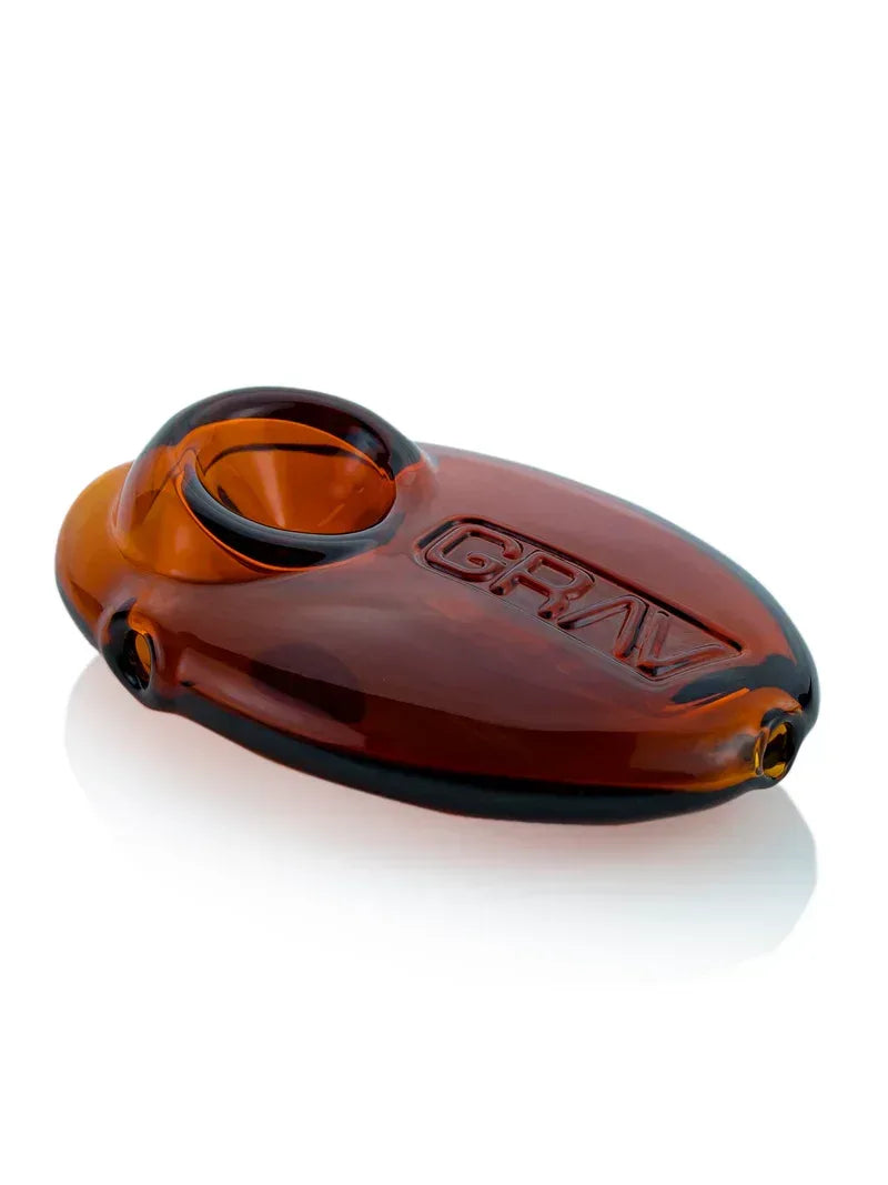 Eine flache, bernsteinfarbene Glaspfeife in ergonomischer Kieselstein-Form mit eingraviertem GRAV-Logo auf einer weißen Oberfläche.