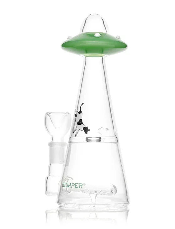 Eine Dreiviertelansicht der UFO-Glasbong mit grünem Raumschiff-Mundstück, schwebendem Kuh-Aufkleber und einem grünen Hemper-Logo auf dem Sockel.