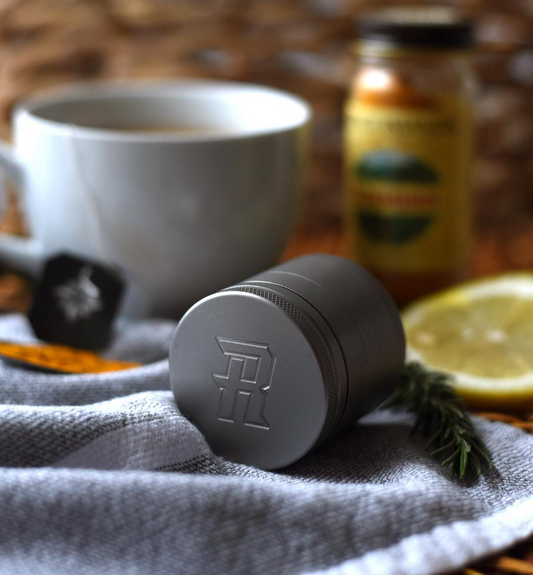 Grinder von The Ripper liegt auf einer Decke. Im Hintergrung eine Kaffeetasse, ein Stück Zitrone.