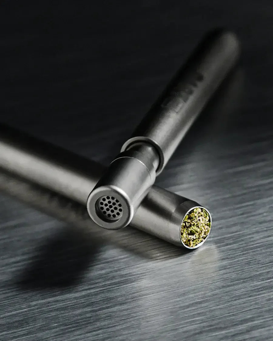 Nahaufnahme von zwei DART One-Hitter-Pfeifen aus Titan, wobei eine das Lochsieb zeigt und die andere mit Kräutern gefüllt ist.