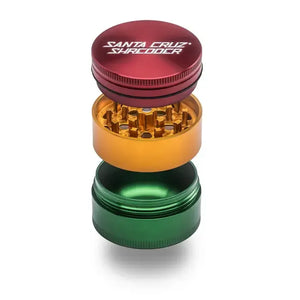 Ein dreiteiliger Santa Cruz Shredder Grinder im Rasta-Farbschema (Rot, Gold, Grün) in einer vertikalen Explosionsdarstellung.